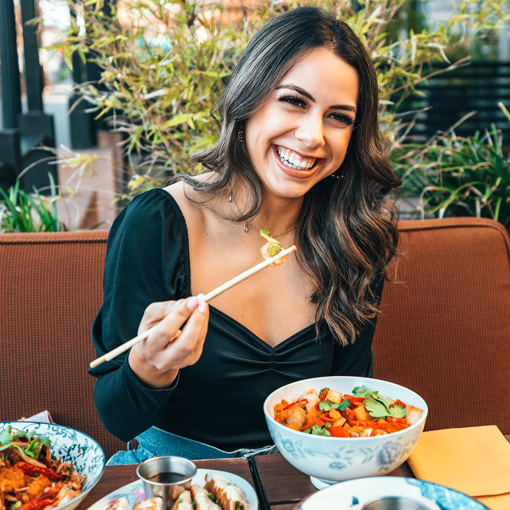 woman smiling while holding chopsticks with food in them.