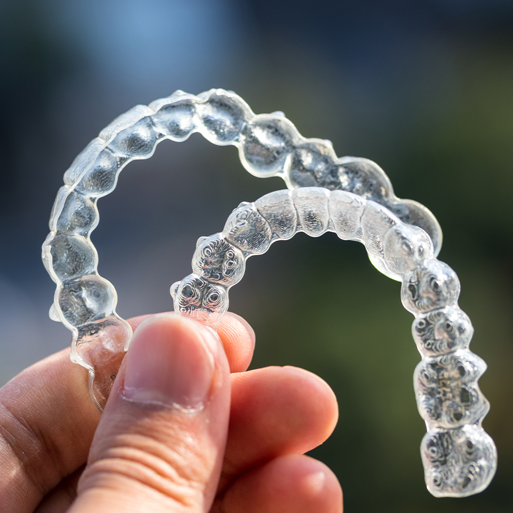 person holding up upper and lower Invisalign liners.
